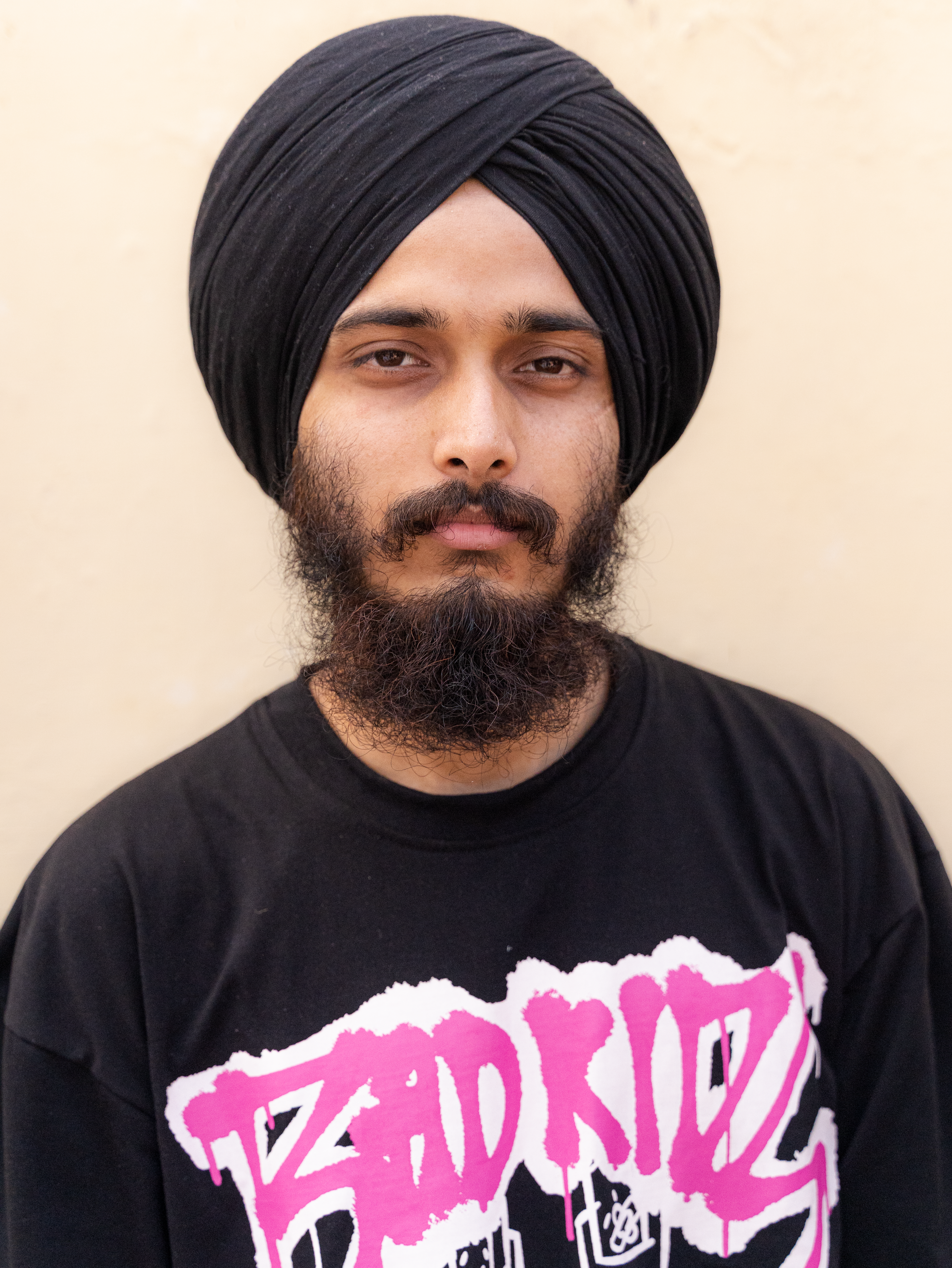Young man with a black turban, beard, and graphic t-shirt posing for a portrait.