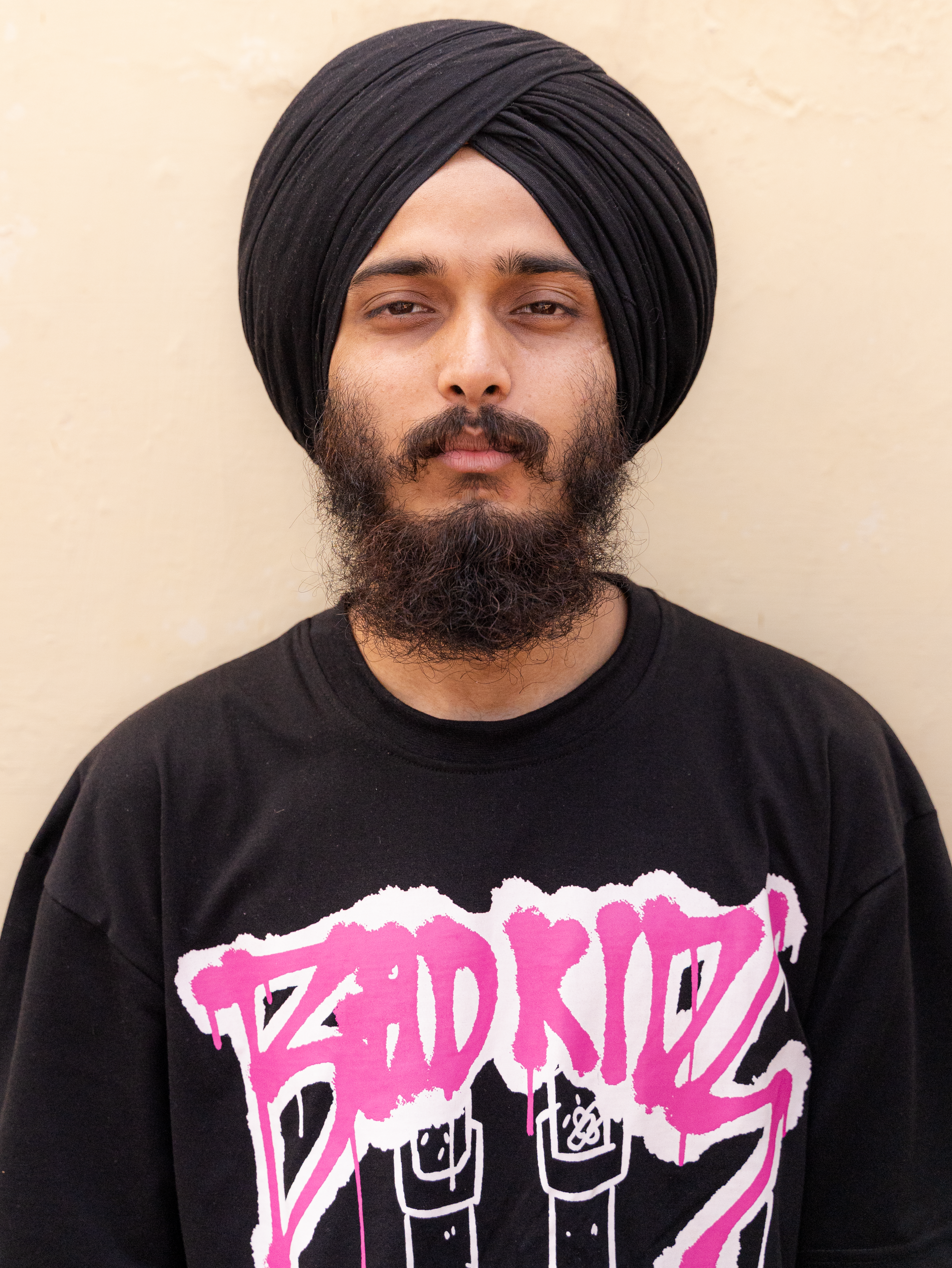 Portrait of a young man with a turban and beard, wearing a bold graphic t-shirt.