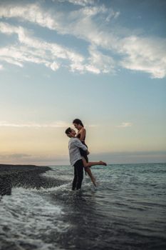 A couple affectionately embracing on the shore during sunset with a beautiful ocean backdrop.