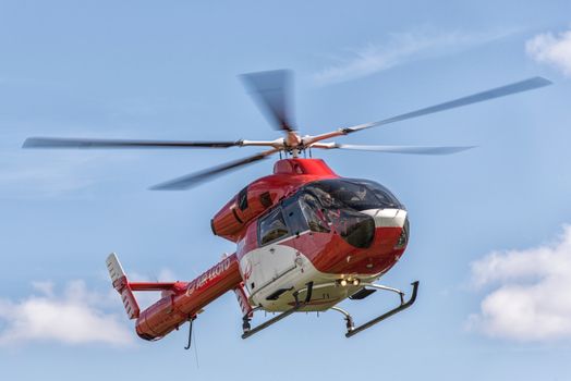 A red helicopter from Air Lloyd flying against a clear blue sky in Hamburg, Germany.
