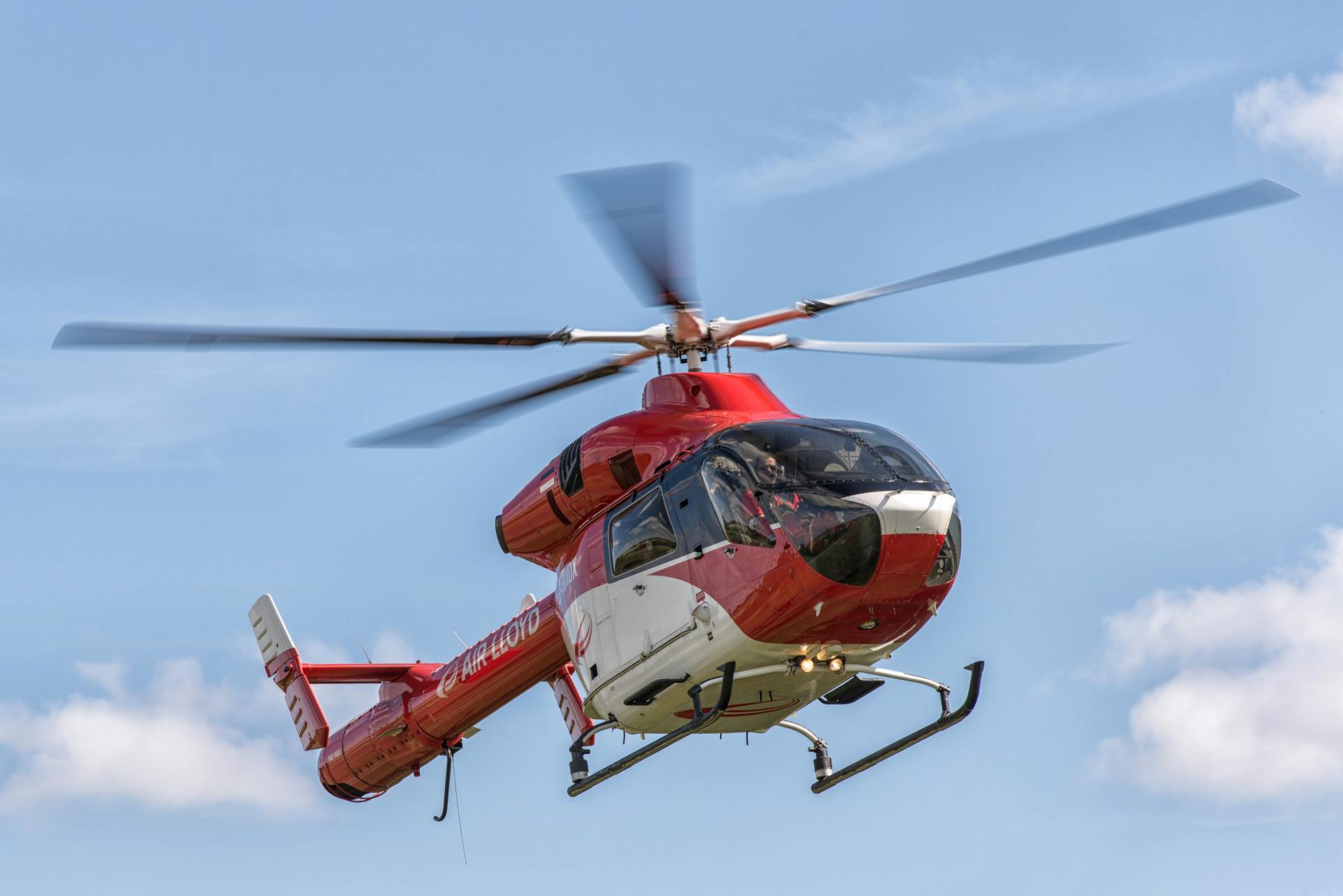 A red helicopter from Air Lloyd flying against a clear blue sky in Hamburg, Germany.