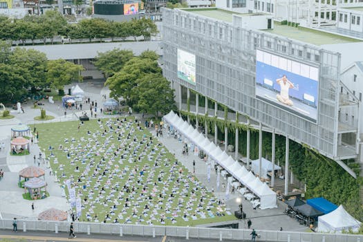 A large group practicing yoga outdoors in Gwangju, South Korea, with an instructor on screen.