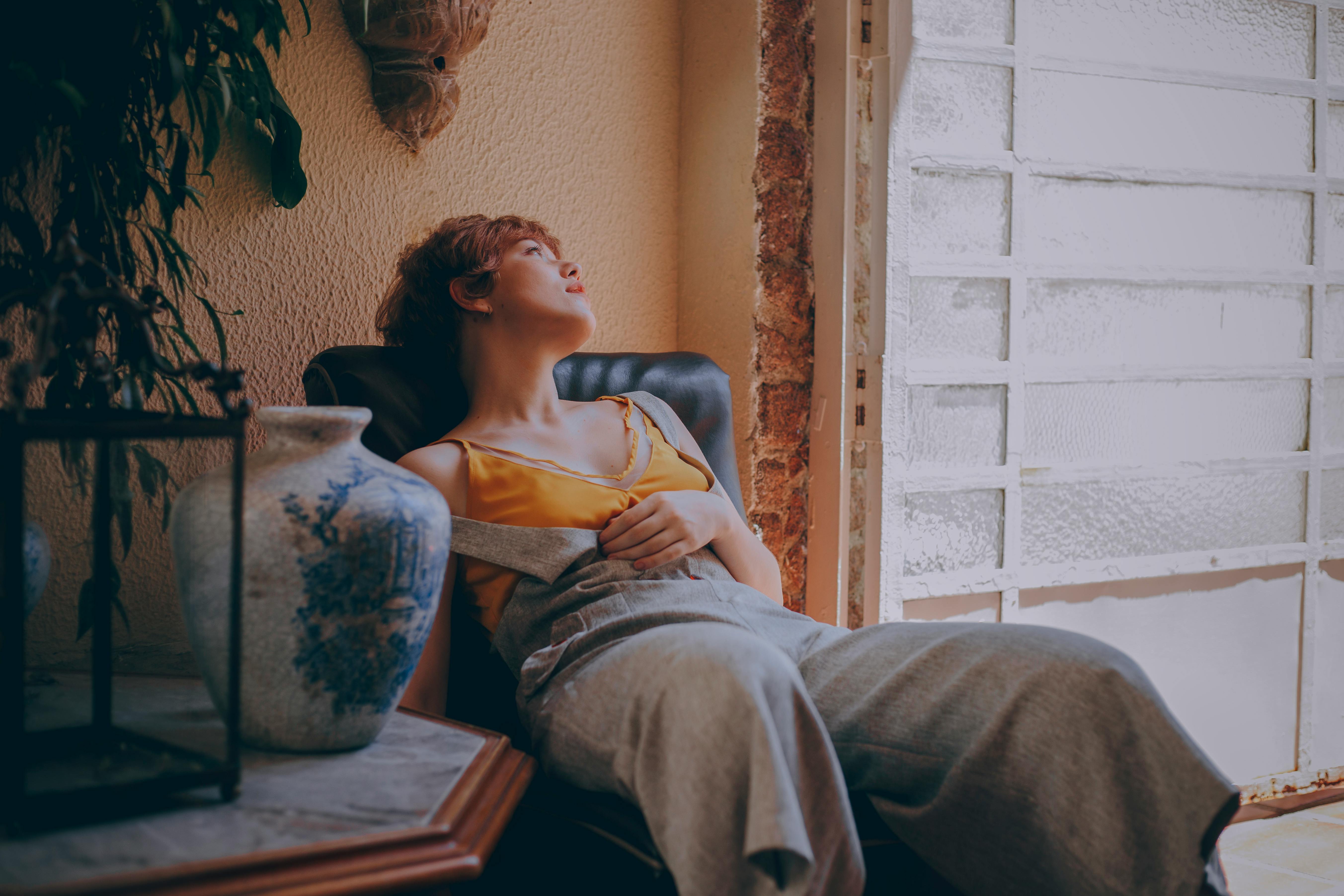 一位女士坐在窗前的椅子上，在舒适而富有艺术气息的室内环境中放松身心