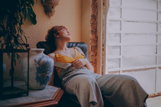 一位女士坐在窗前的椅子上，在舒适而富有艺术气息的室内环境中放松身心