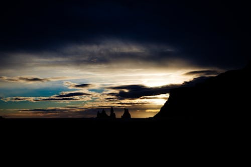 Silhouette of Rock Formations Under Cloudy Sky