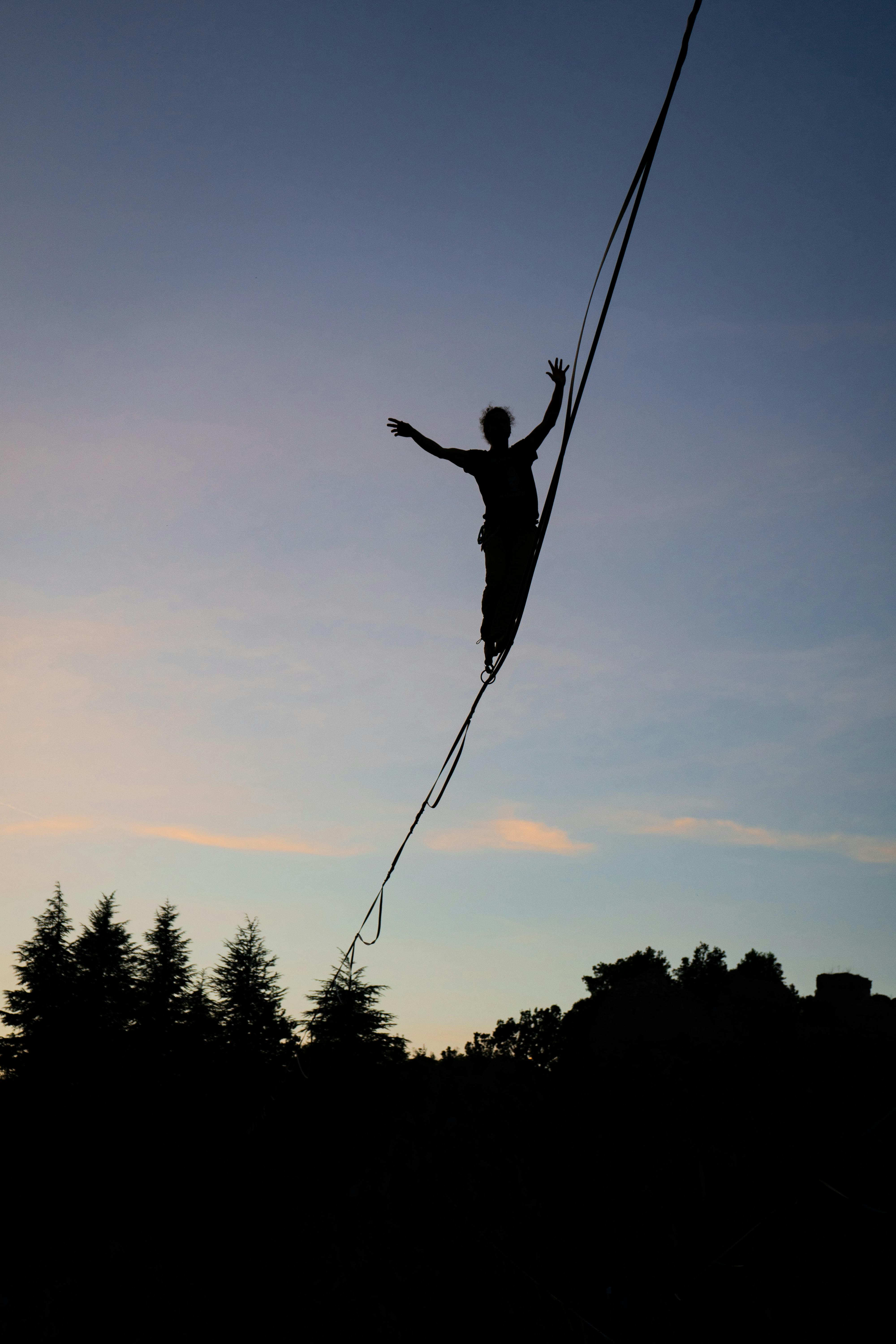 Silhouette of a Person Balancing on a Tightrope at Dusk · Free