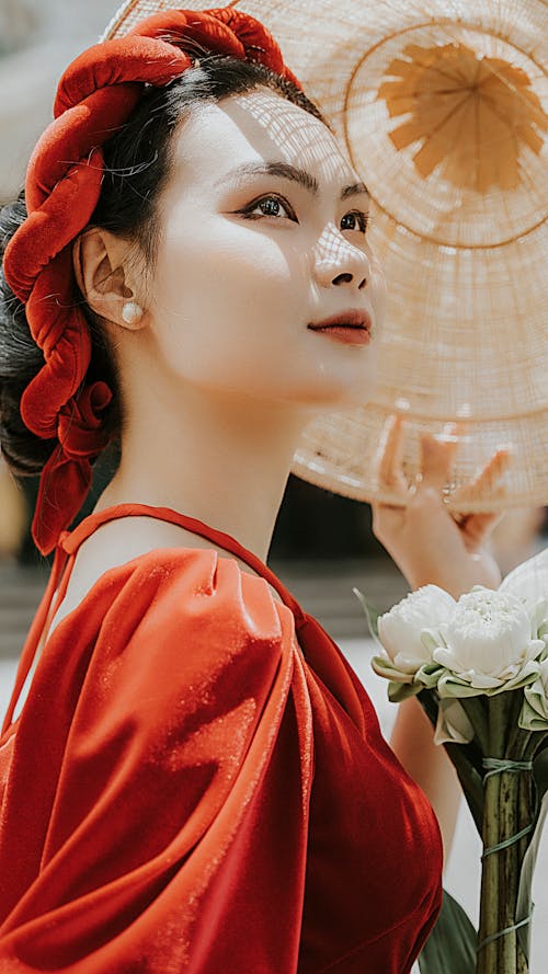 Young Woman in Red Dress and Headband Holding a Straw Hat and Flower Bouquet