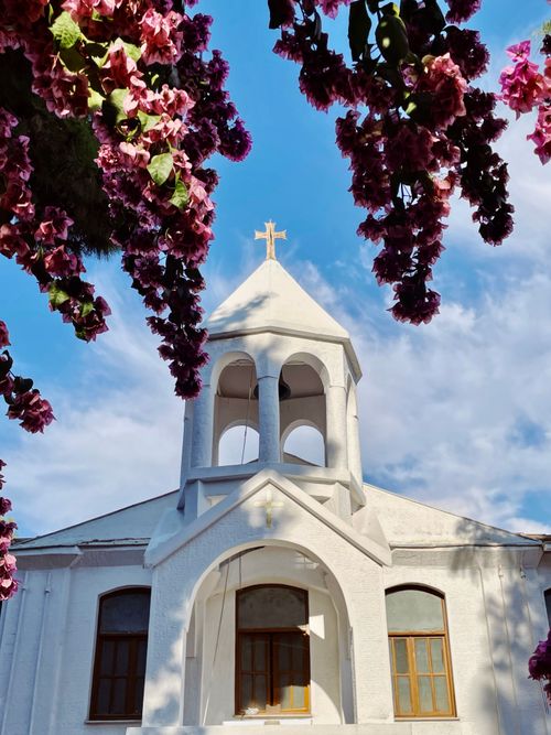 Free White church facade framed by vibrant pink blossoms under a clear spring sky. Stock Photo