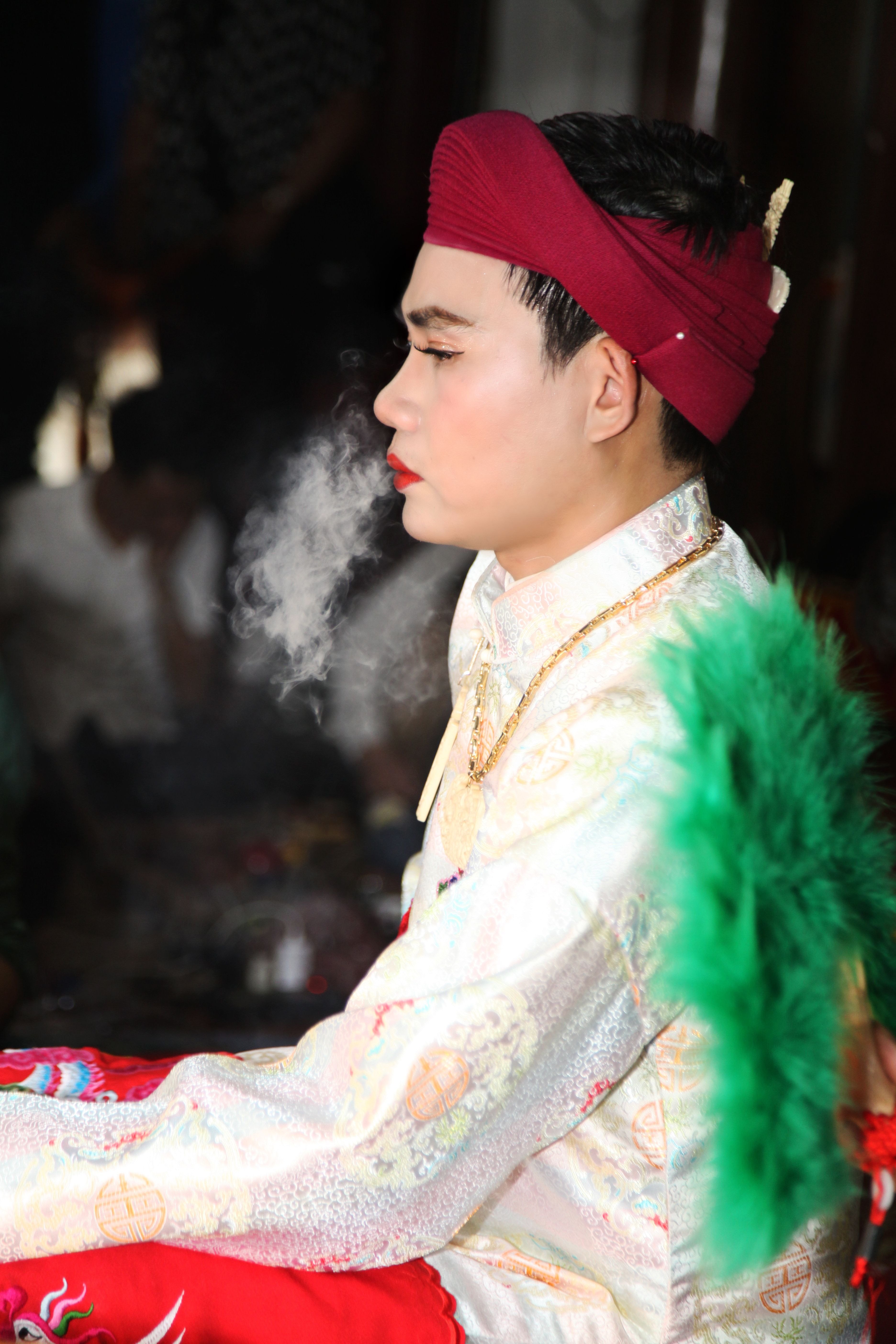 A young Asian man in ceremonial attire during a traditional ritual, smoking incense.