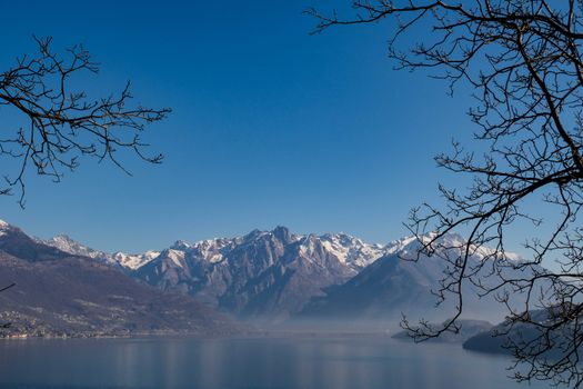 Breathtaking view of snowy mountains reflected in a serene lake, framed by winter trees.
