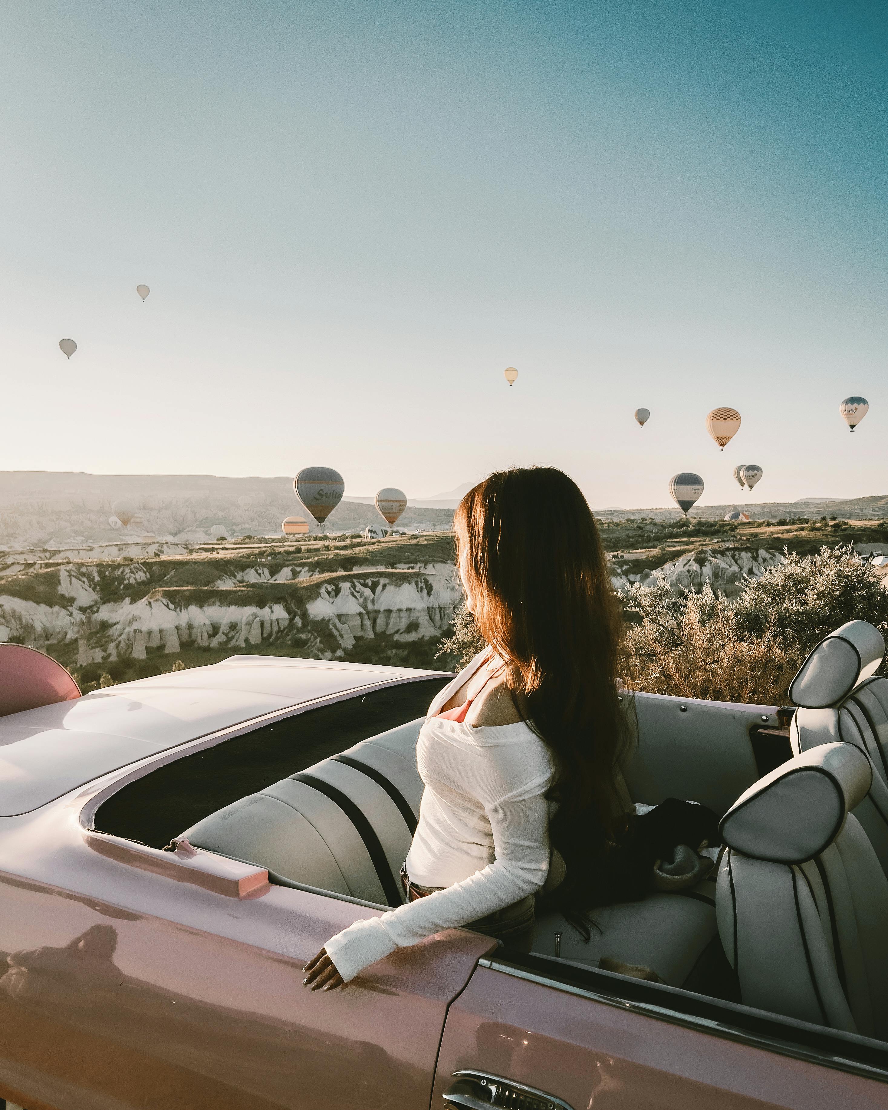 Free A woman in a convertible enjoying hot air balloons at sunrise over Cappadocia's scenic landscape. Stock Photo