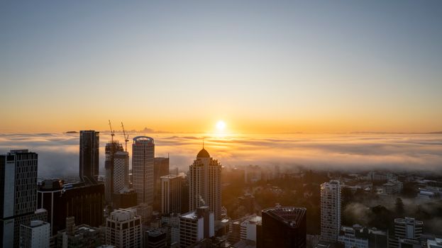 Auckland city skyline enveloped in fog during a beautiful sunrise.