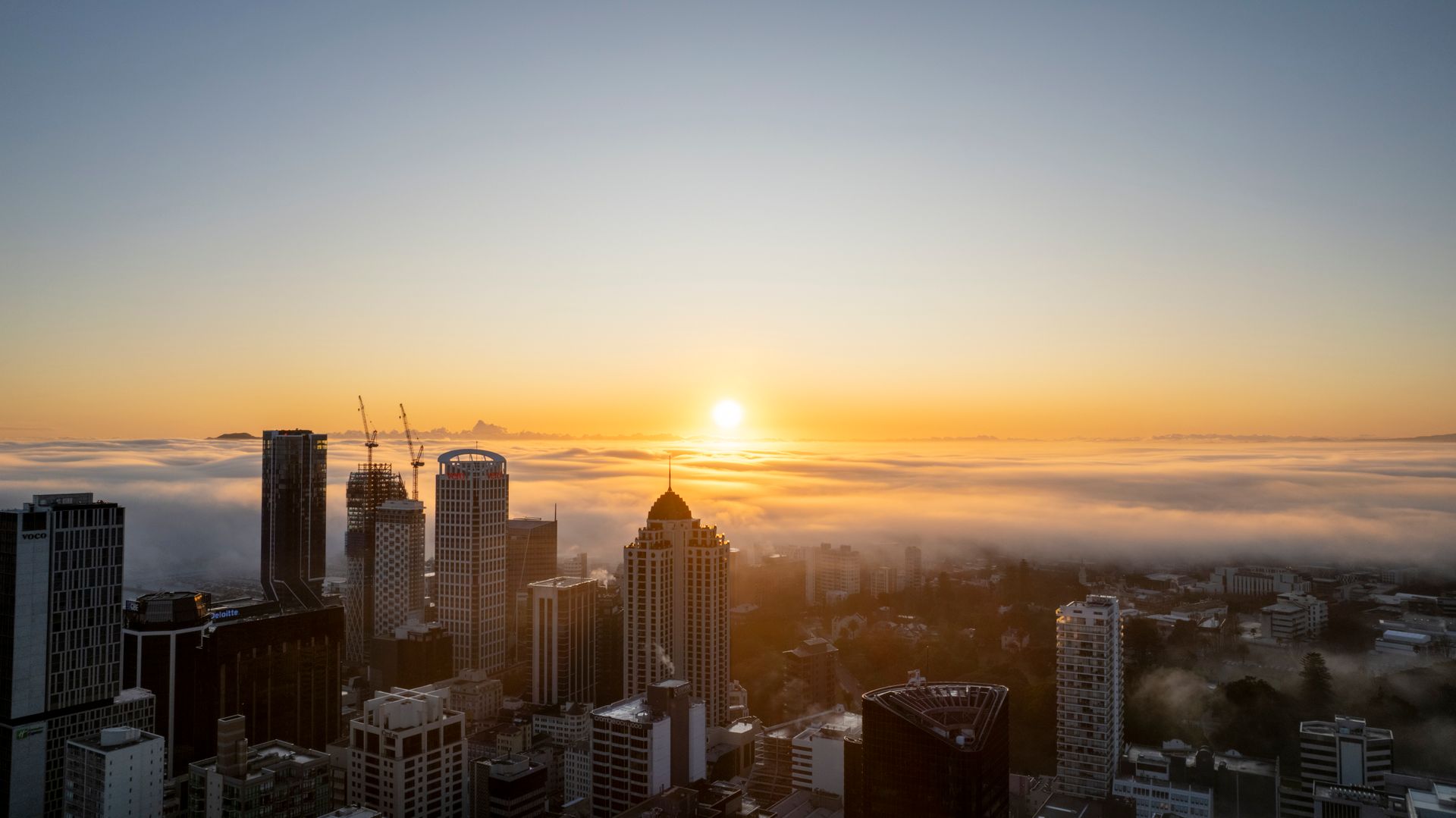 Auckland city skyline enveloped in fog during a beautiful sunrise.