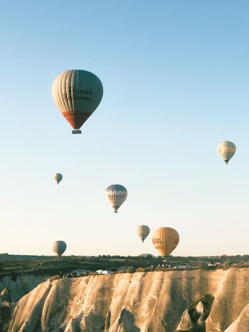 Free Scenic view of colorful hot air balloons floating over the rocky cliffs of Cappadocia, Turkey during sunrise. Stock Photo