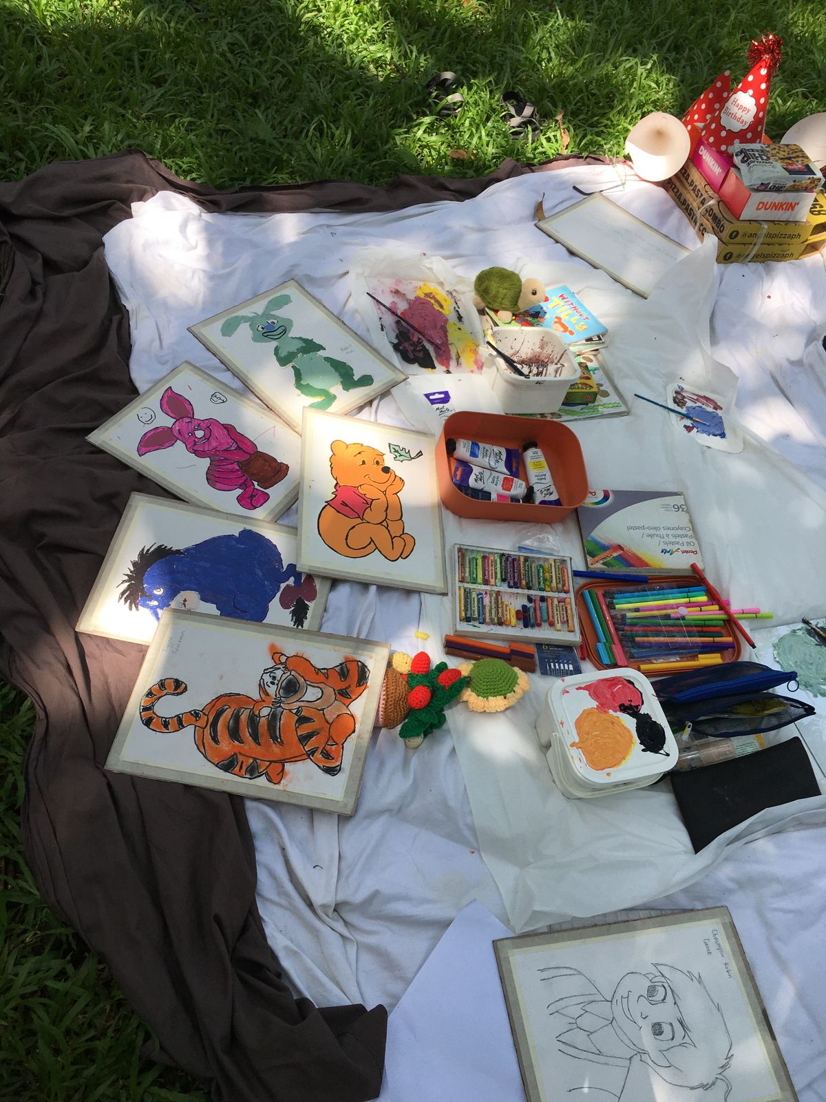 Outdoor art setup with children's drawings and supplies on a blanket for a rainbow bird