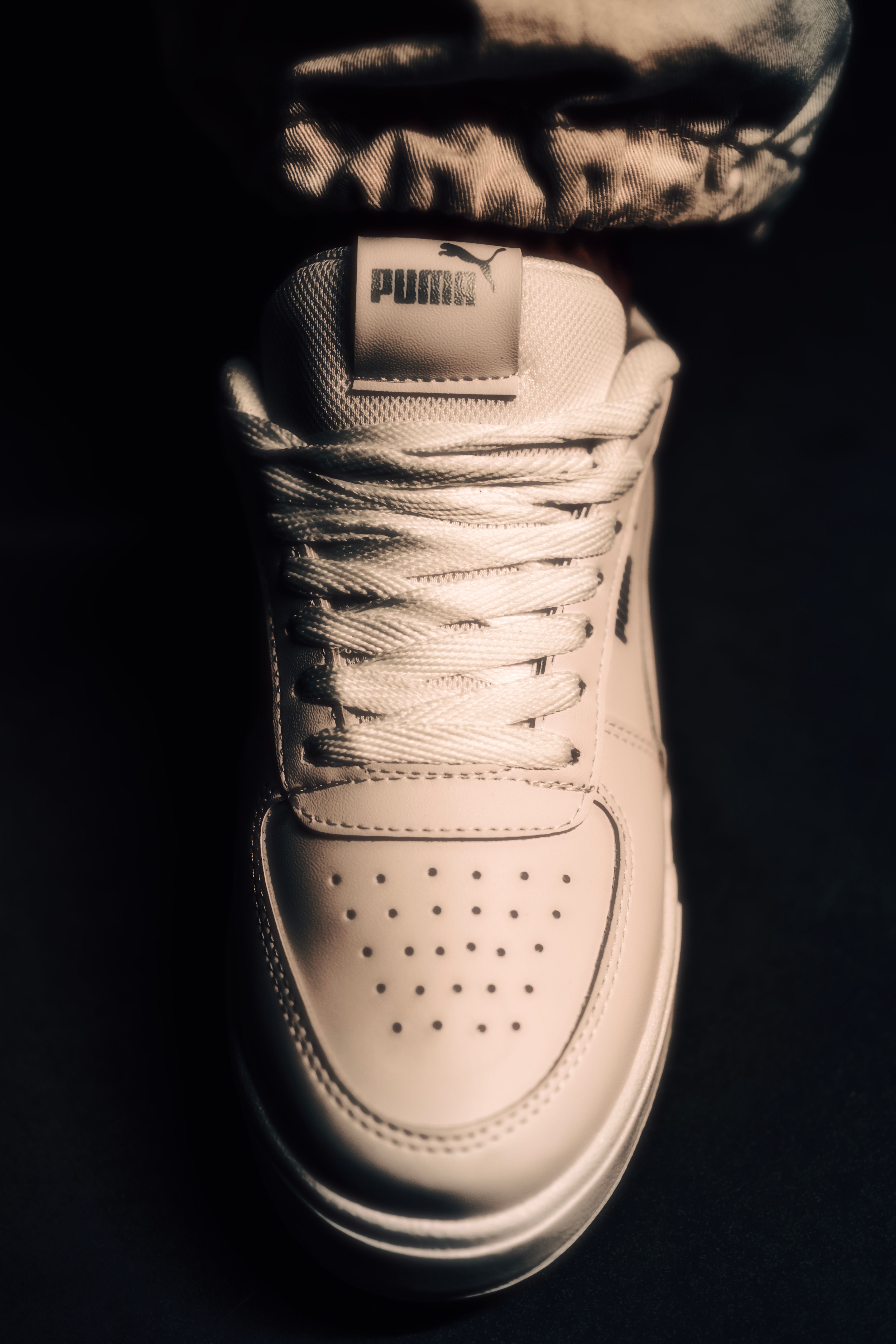 Close-up of a white Puma sneaker on a dark background, highlighting fashion and footwear details.