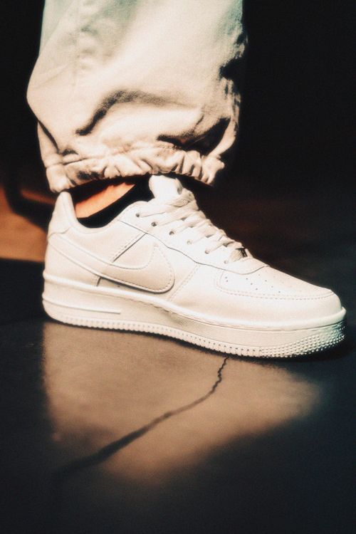 Free Fashion-forward close-up of white sneakers on a textured floor showcasing footwear style. Stock Photo