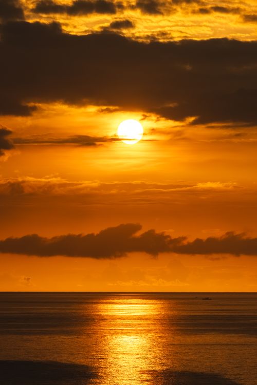 Free Stunning sunset casting warm hues over tranquil ocean with dramatic clouds. Stock Photo