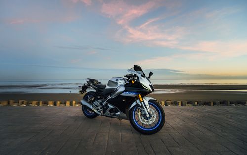 Free A sleek sports motorcycle parked by the serene beach during sunset with vibrant sky. Stock Photo