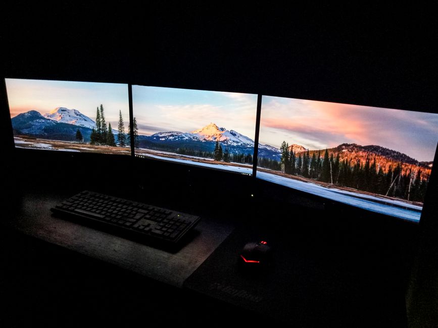 Contemporary computer with picturesque nature photos on monitors near keyboard and mouse in dark room