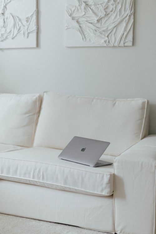 Free A minimalist living room featuring a white sofa and a laptop, showcasing a clean and simple aesthetic. Stock Photo