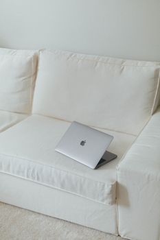 Sleek silver laptop on a clean white sofa in a minimalist setting, ideal for tech or modern lifestyle themes.