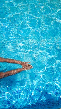 Hands enjoying a refreshing swim in a bright blue pool, perfect for vacation vibes.
