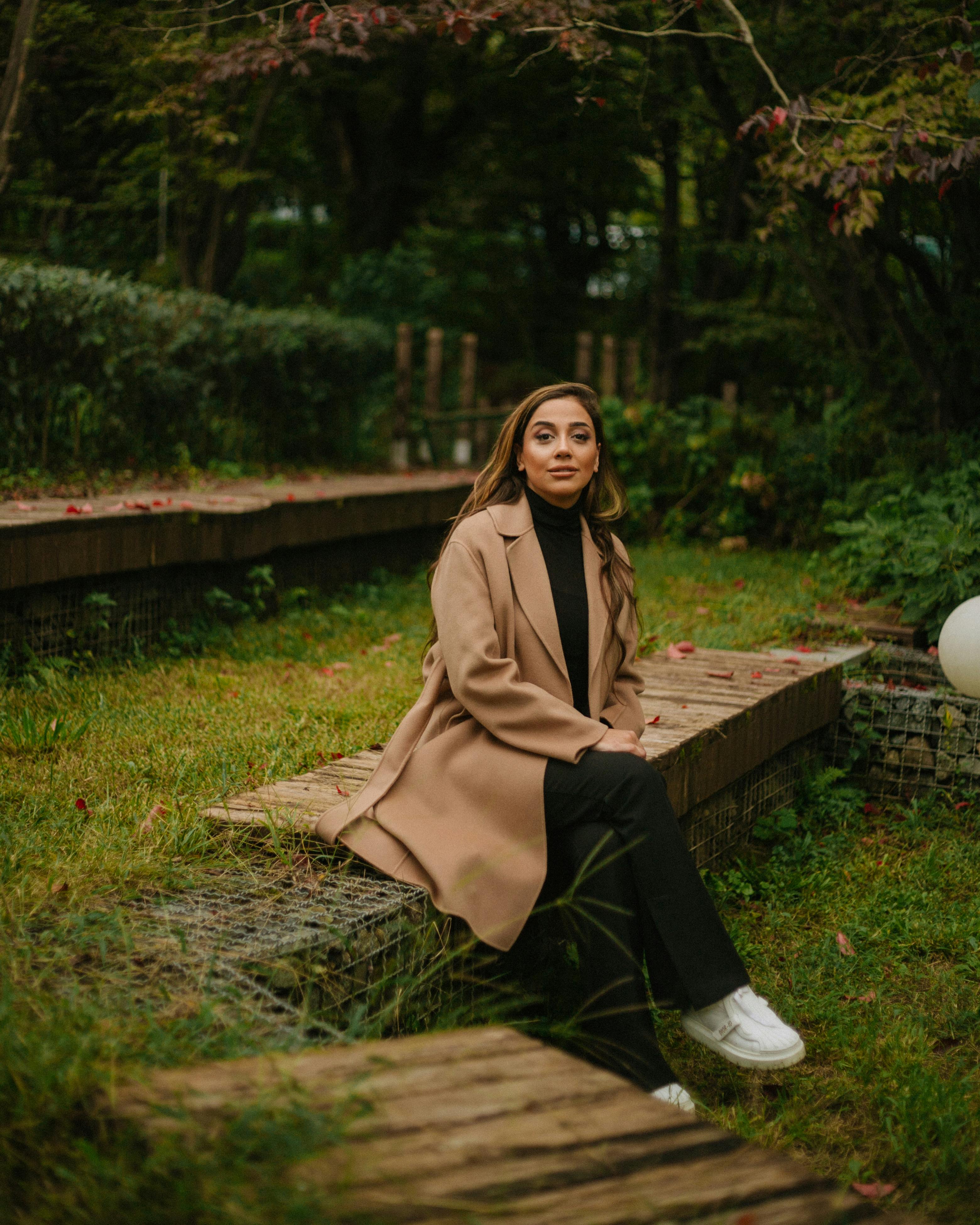 Stylish woman wearing a woolen coat sits in a scenic autumn park in Baku, Azerbaijan.