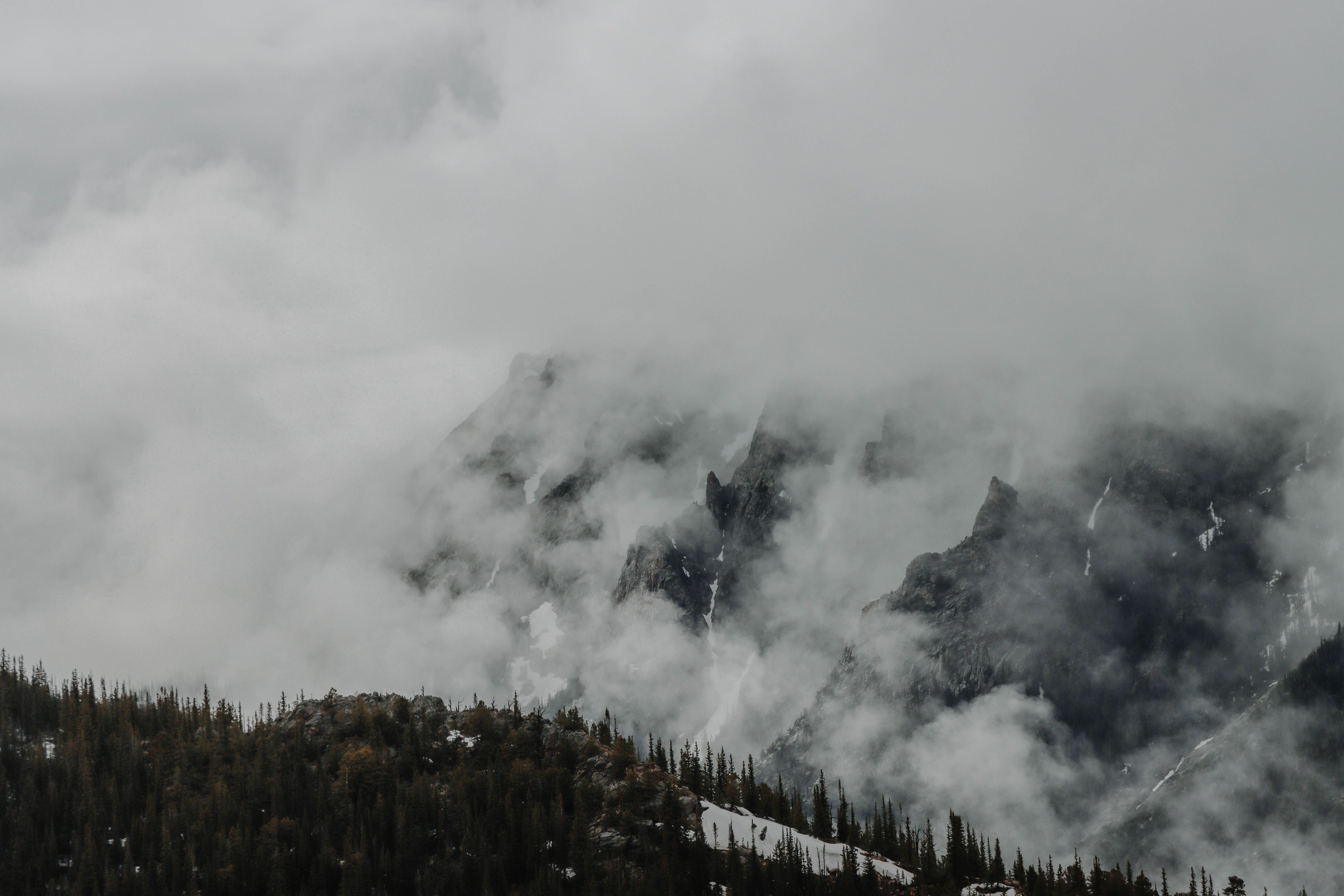 A dramatic view of the Rocky Mountains shrouded in mist and clouds, creating a mysterious atmosphere.