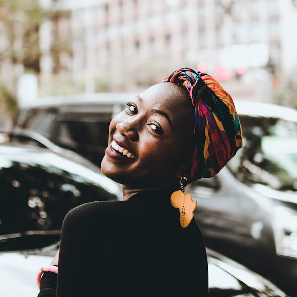 woman wearing a headwrap and an Africa-shaped earring while smiling