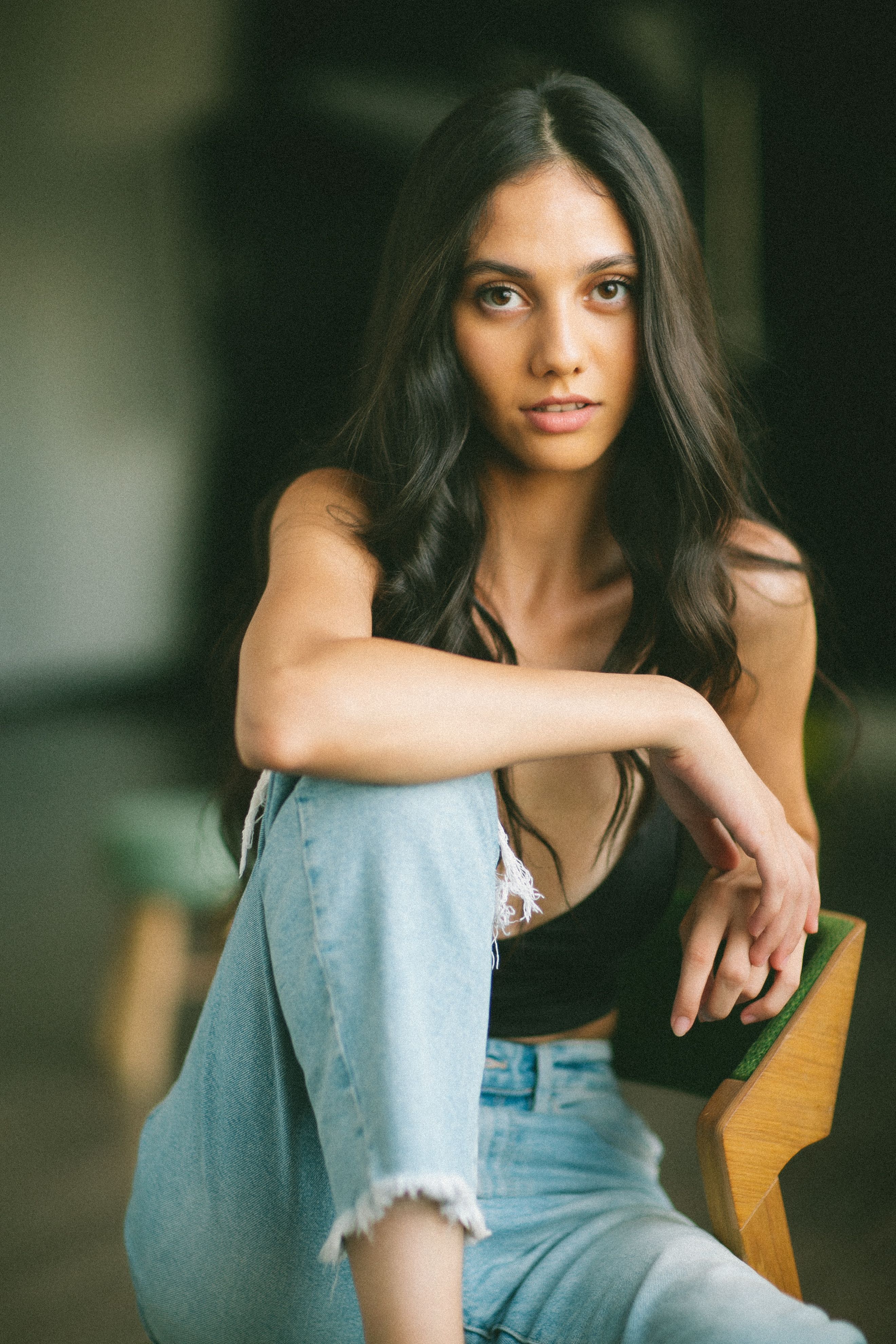 A casual portrait of a woman in jeans, posing comfortably indoors with a warm, relaxed expression.