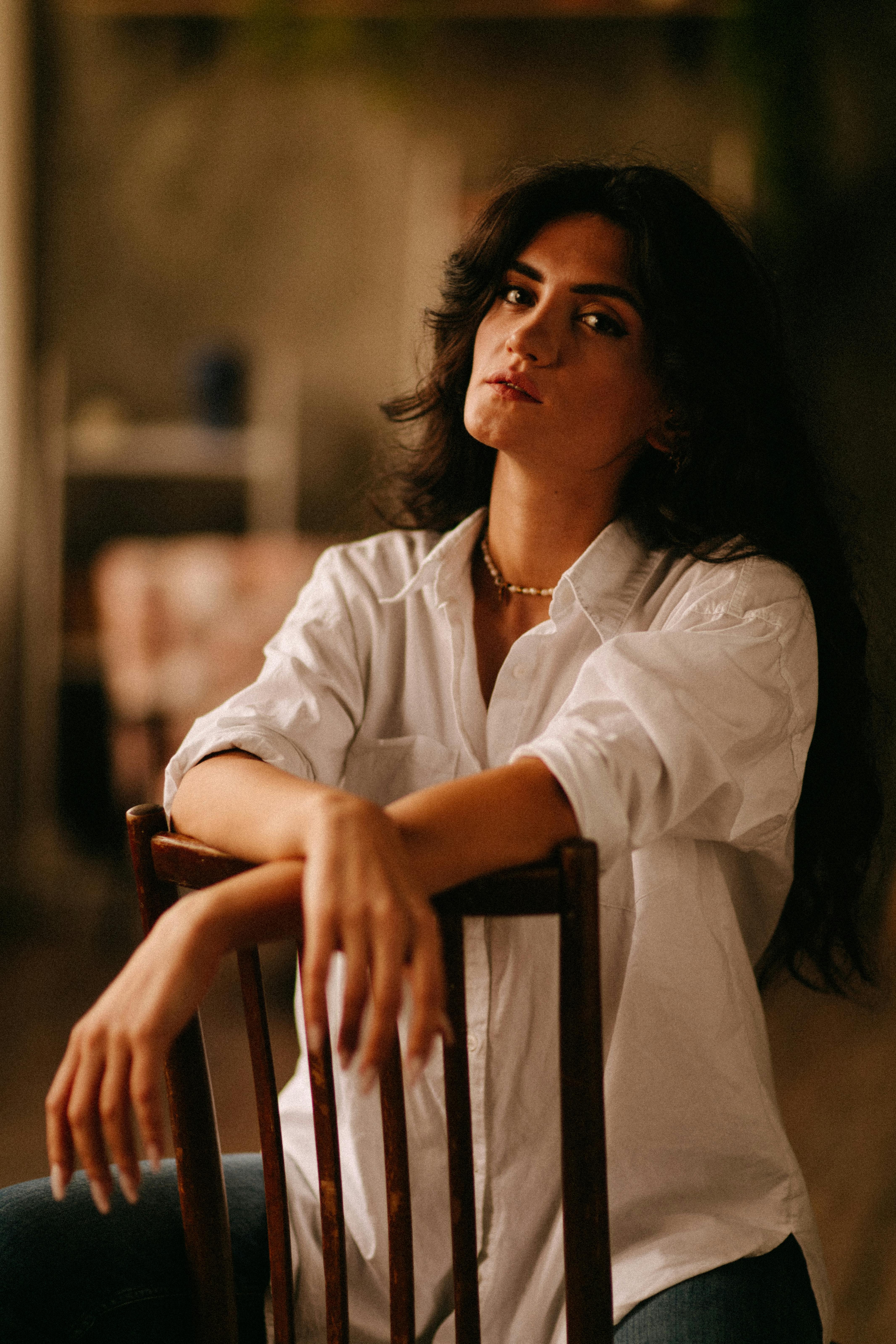 Portrait of a woman sitting on a chair, wearing a white blouse indoors.