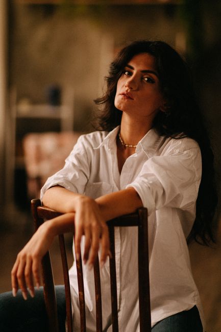 Portrait of a woman sitting on a chair, wearing a white blouse indoors.