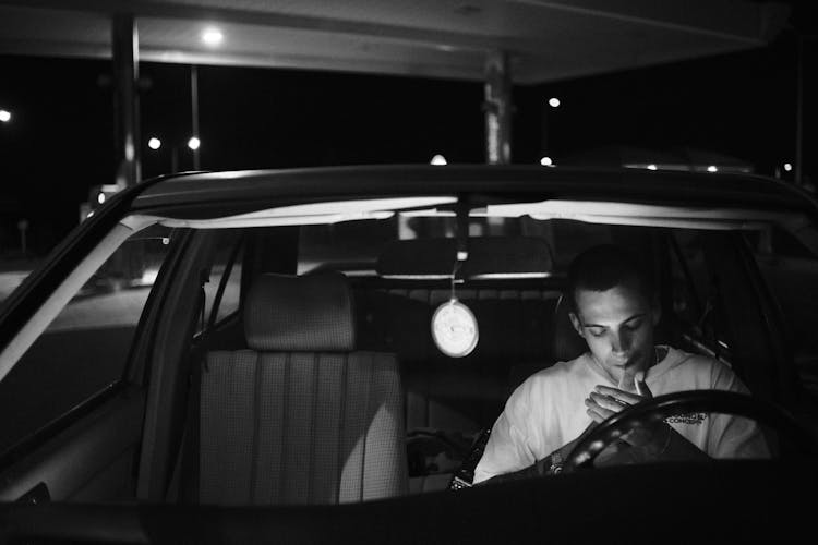 Young Man Sitting In A Car And Lighting A Cigarette 