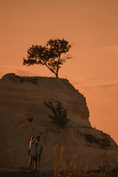 A couple embraces atop a hill under a striking orange sunset, symbolizing romance and adventure.