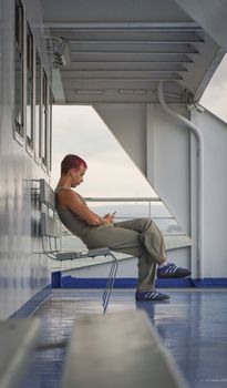 A young adult with dyed hair using a smartphone while sitting on a ferry in Istanbul, Türkiye.