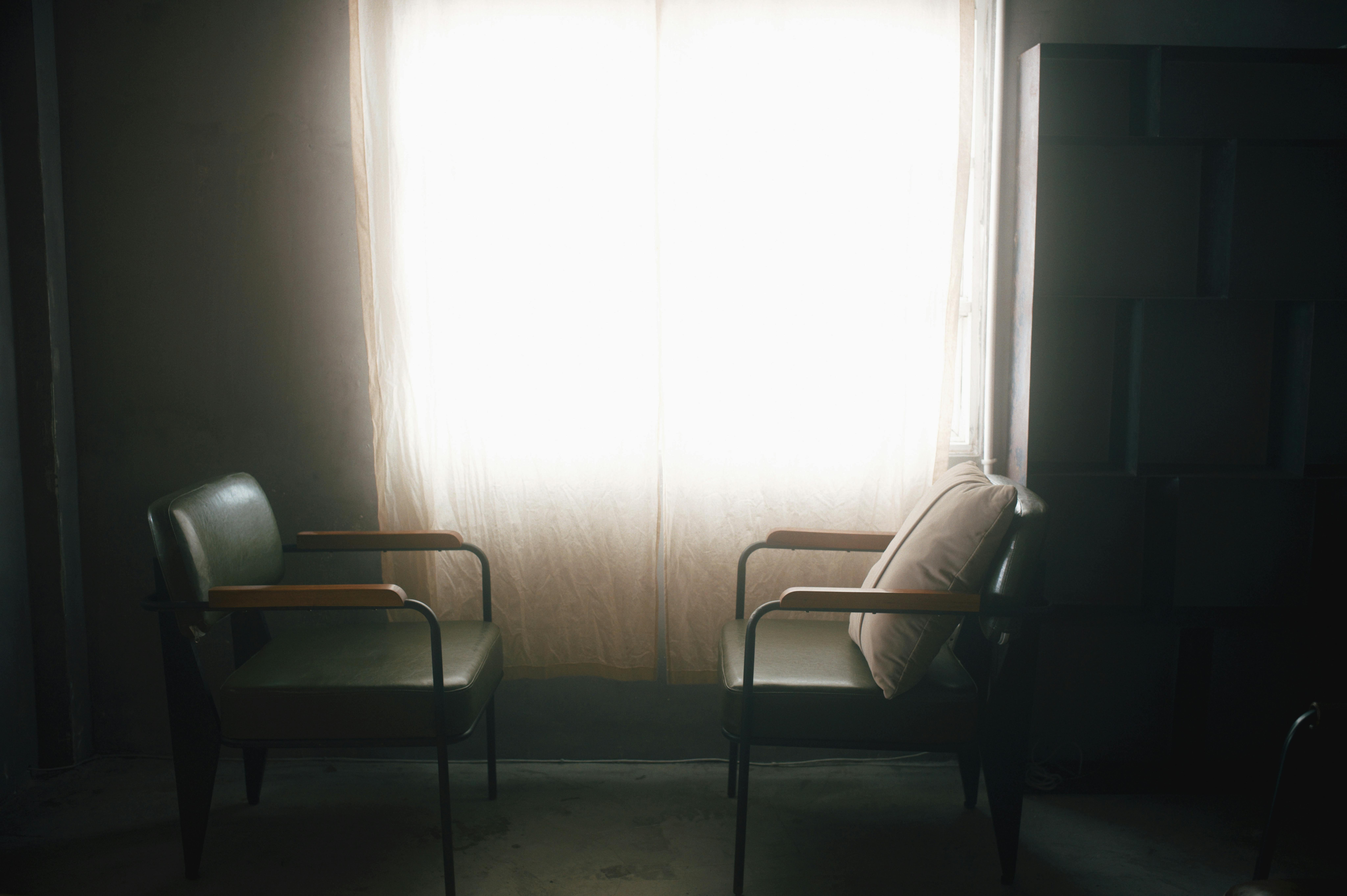 A tranquil indoor scene with two empty leather armchairs in front of a softly lit curtained window.