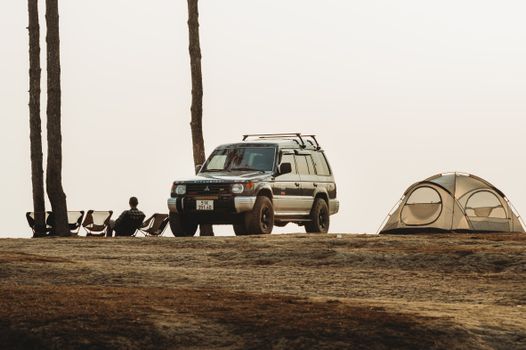 A serene outdoor camping scene featuring an SUV, tent, and chairs among tall trees.