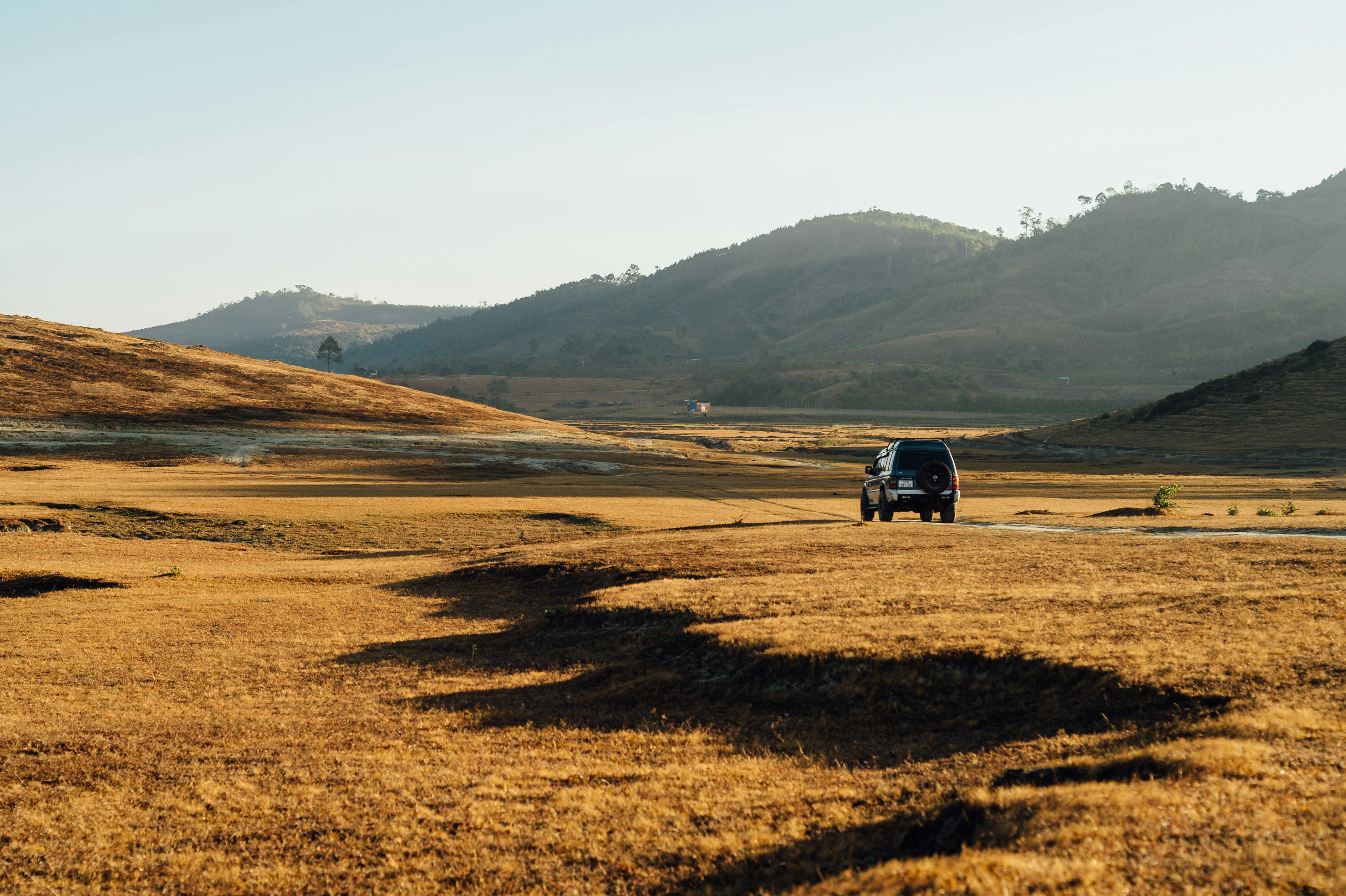 A 4x4 vehicle driving through a vast rural countryside under clear skies.