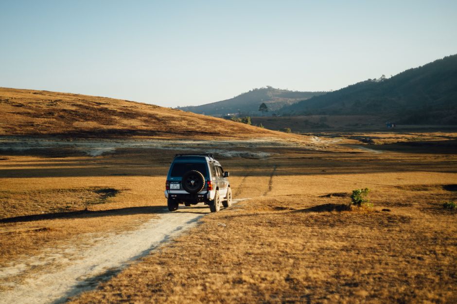 SUV traveling on a dusty path in a remote, barren landscape under clear sky.