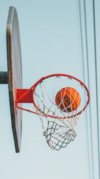 Captured mid-action, a basketball goes through the hoop against a clear sky background.