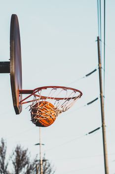 Basketball going through a hoop outdoors on a clear day, symbolizing victory and sport.