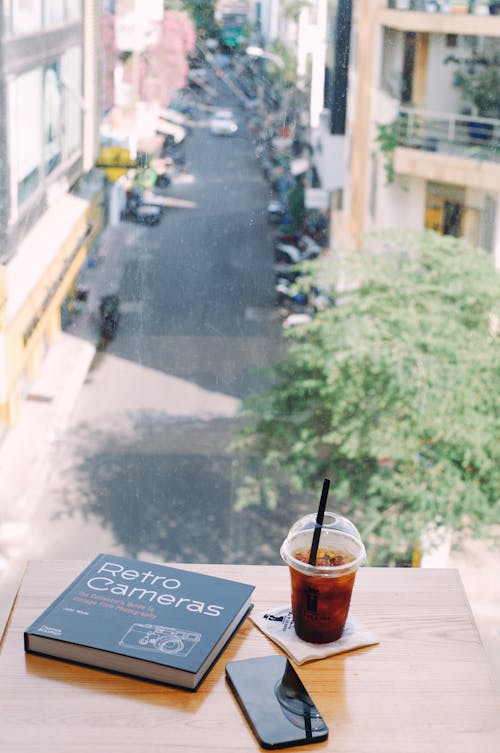 A Coffee, a Book and a Smartphone Lying on the Table in a Cafe with the View of the Street 