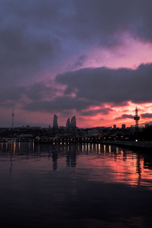 Free Dramatic sunset over Baku's skyline featuring the iconic Flame Towers reflecting on the Caspian Sea. Stock Photo