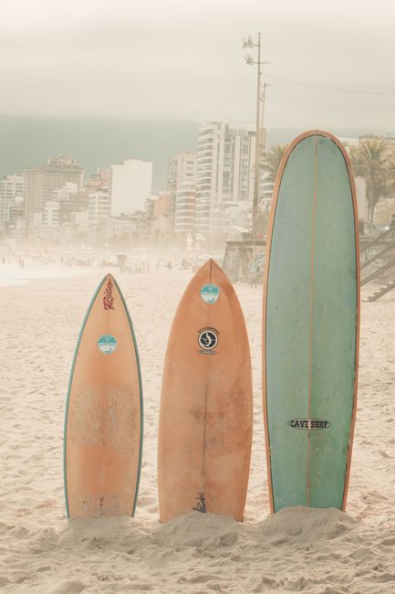 Vibrant surfboards stand on the sandy beach of Rio with urban skyline in the background.