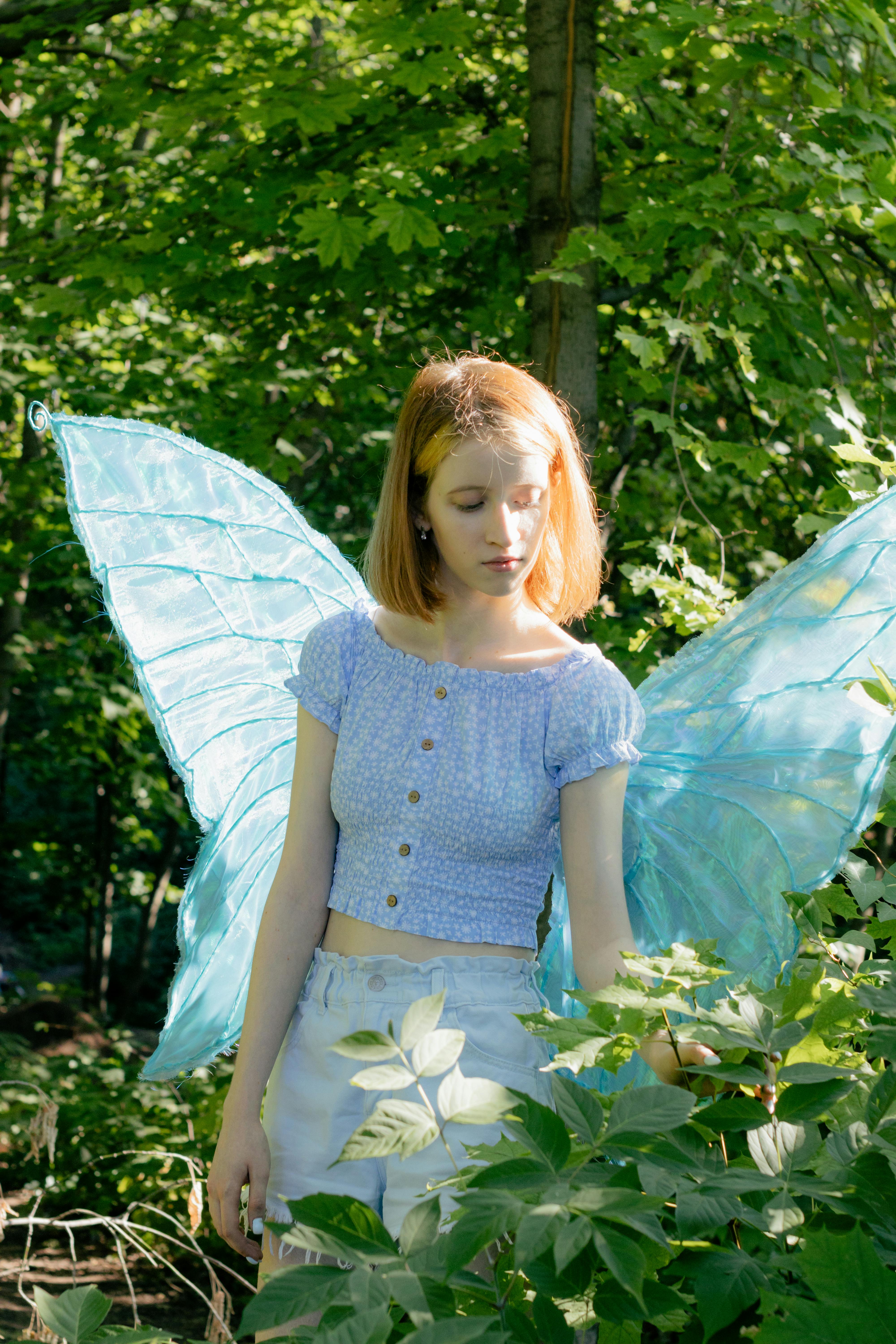 Woman in fairy costume with wings amidst forest foliage in sunlight.