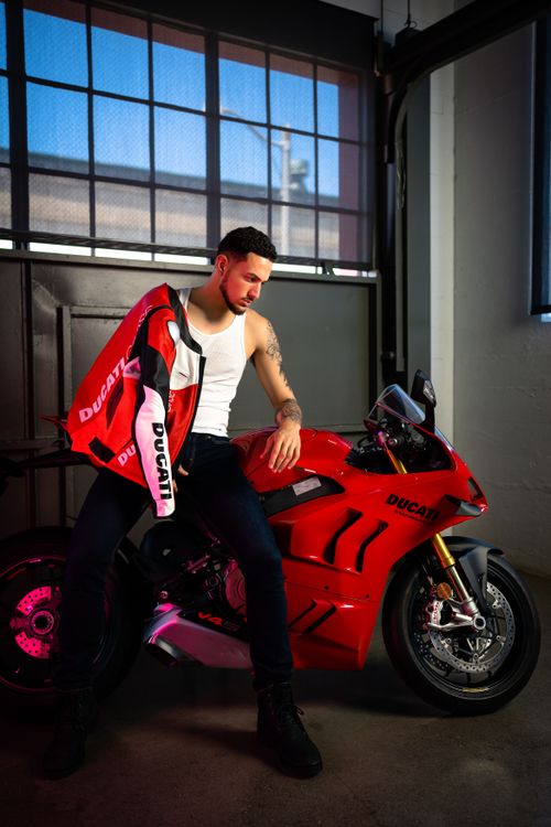Free A fashionable male model poses with a red motorcycle in an indoor setting, exuding modern style. Stock Photo