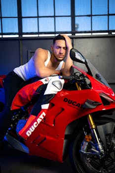 A man posing confidently with a stylish red Ducati motorcycle indoors.