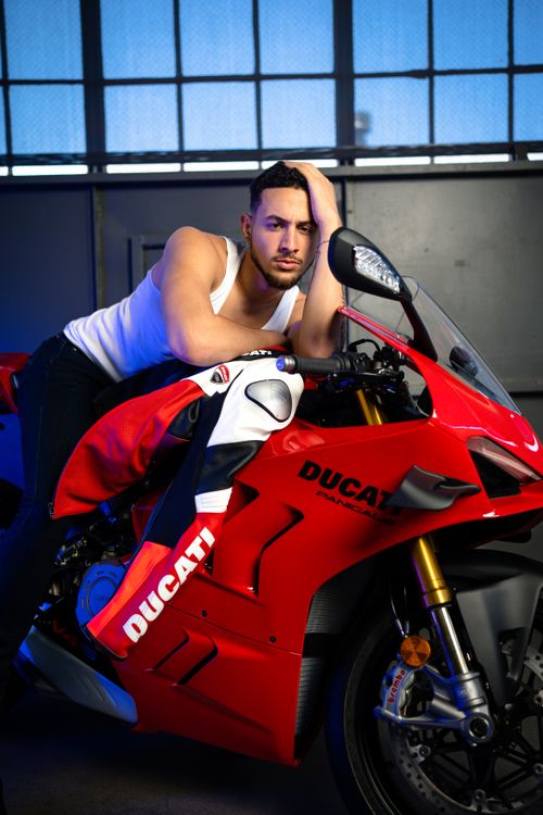 Free A man posing confidently with a stylish red Ducati motorcycle indoors. Stock Photo