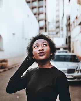 一位留着非洲发型的年轻女子在城市街道上若有所思地仰望天空